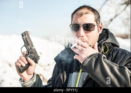 Agente di polizia e guardia del corpo in posa con la pistola e la sigaretta sulla outdoor tiro a segno Foto Stock