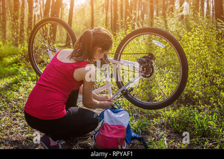 Giovane donna la riparazione di una bicicletta nella foresta al tramonto Foto Stock