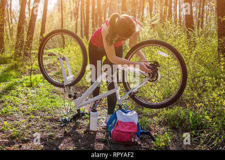 Giovane donna la riparazione di una bicicletta nella foresta al tramonto Foto Stock