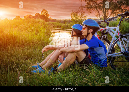 Paio di ciclisti avente il resto dal fiume al tramonto Foto Stock