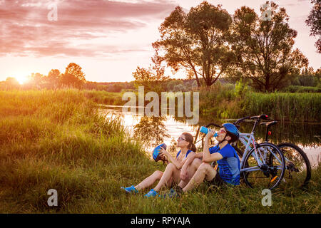 Paio di ciclisti avente il resto dal fiume al tramonto Foto Stock