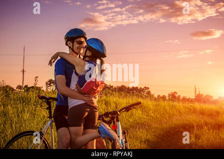 Paio di ciclisti abbracciando dopo di equitazione in periferia al tramonto. Attiva uno stile di vita sano. Giovani motociclisti viaggiare insieme Foto Stock
