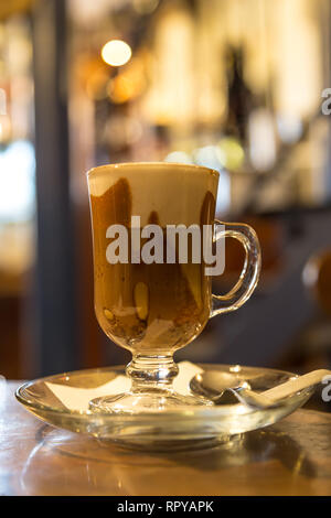 Marocchino caffè servito in un bicchiere piccolo con un tiro di espresso, il cacao in polvere e del latte con la schiuma. Foto Stock