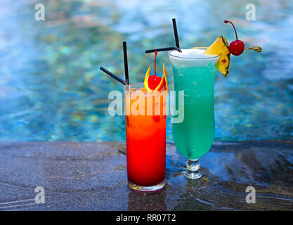 Vetro con un luminoso laguna blu e Tequila Sunrise cocktails presso la piscina. Resort di lusso sull'isola tropicale Foto Stock