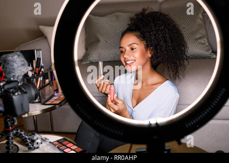 Sorride mostrando vlogger rossetto spazzola durante la registrazione di un video Foto Stock