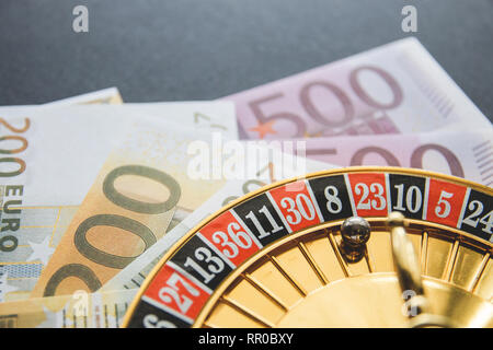 Gold Casino tema. Immagine del casino, Roulette Giochi del poker, il denaro sul tavolo, tutti su un bokeh di fondo scuro dello sfondo. Posto per la stampa di logo e. Foto Stock