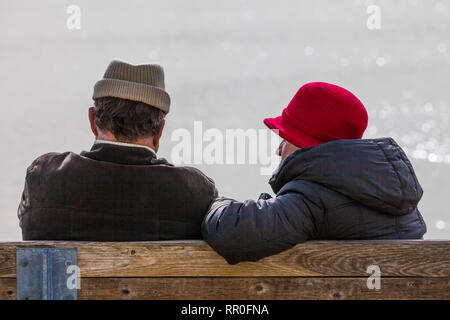 Coppia di anziani in conversazione su una panchina sul lungomare in inverno Foto Stock