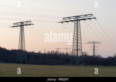 Grande raccolta di tralicci di energia elettrica con i cavi, essi sono sfalsati come sagome di fronte un lievemente colorata del cielo della sera nella zona in prossimità di un bi Foto Stock