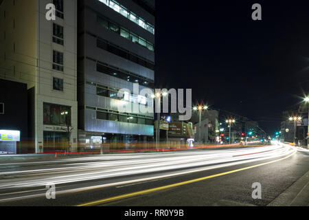 Fari di automobili su una strada trafficata a Hiroshima, Giappone, di notte Foto Stock