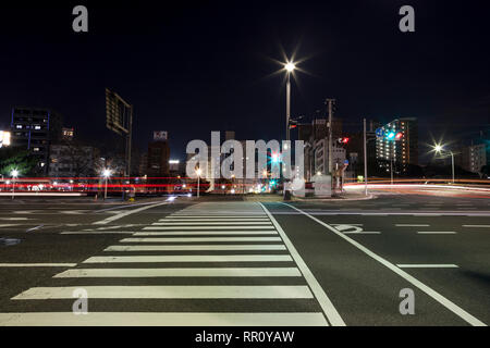 Attraversamento pedonale e il semaforo di attraversamento di Fiume nei pressi di Hiroshima principale stazione ferroviaria di notte, con sentieri di luce dai veicoli in transito Foto Stock