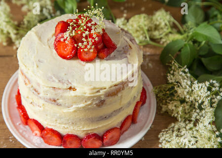 Torta con un bianco crema al cioccolato e fragole con anziano sul tavolo di legno Foto Stock