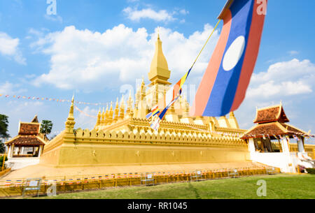 (Fuoco selettivo) Alcuni Laos bandiere sventolano in primo piano con la sfocato Pha That Luang in background. Foto Stock