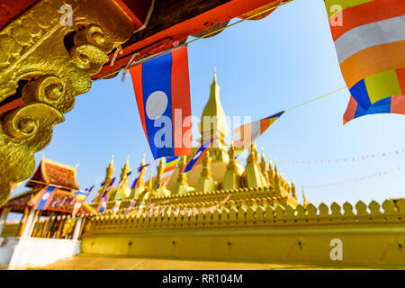 (Fuoco selettivo) Alcuni Laos bandiere sventolano in primo piano con la sfocato Pha That Luang in background. Foto Stock