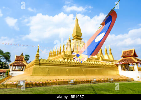 (Fuoco selettivo) Alcuni Laos bandiere sventolano in primo piano con la sfocato Pha That Luang in background. Foto Stock