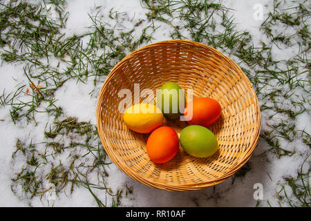 Cinque colorate uova di pasqua in un cesto di paglia sulla sommità di neve ed erba isolato caccia all'uovo Foto Stock