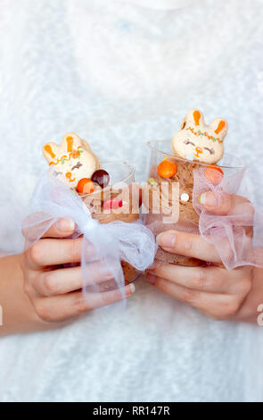 Donna di mani che tengono in plastica trasparente cup con mousse di cioccolato, decorata con bunny cookie sagomato Foto Stock