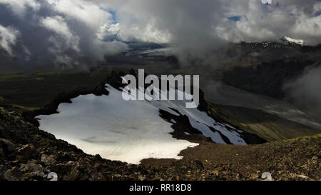 Vista dalla montagna di oltre il patch di neve e la valle sottostante con le nuvole sopra di esso in Skaftafell national park nel sud dell'Islanda. Foto Stock