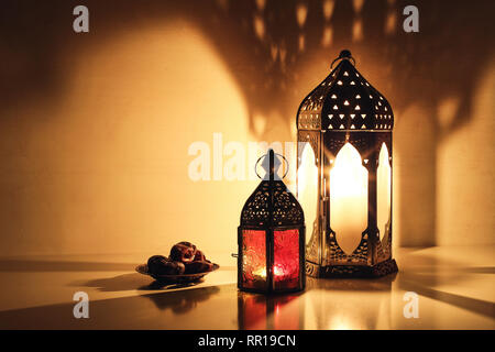 Ornamentali lanterne arabo con candele accese incandescente durante la notte. Piastra con data di frutta sul tavolo. Messaggio di saluto festivo card, invito per musulmani Foto Stock