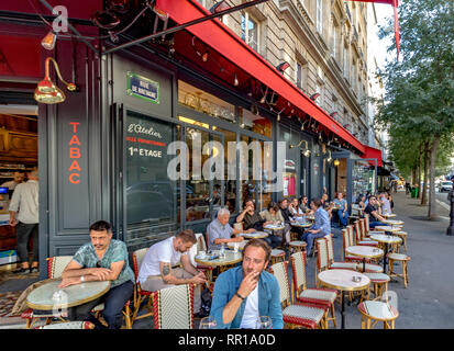 Un uomo che fuma una sigaretta seduta fuori sul marciapiede in un bar ristorante in Rue de Bretagne, Parigi, Francia Foto Stock