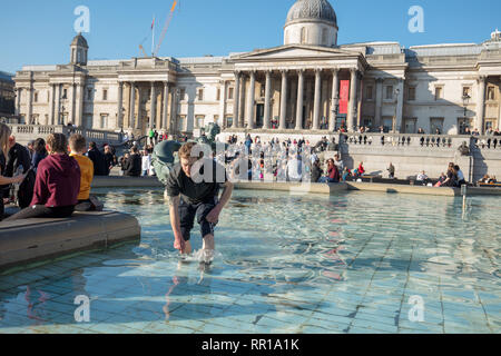 Uomo senza tetto alla ricerca di monete in acqua della fontana in Trafalgar Square. Turisti e visitatori di godersi il caldo molla come meteo in febbraio Foto Stock