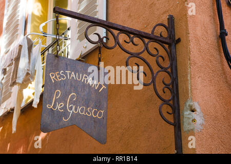 Insegna vintage in ferro battuto per il Restaurant Le Guasco montata su un muro arancione lungo una strada panoramica a Bastia, Corsica, Francia. Foto Stock