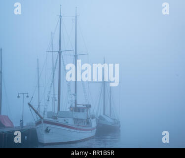 Misty romantico di imbarcazioni a vela senza vele in acqua vicino a un dock Foto Stock