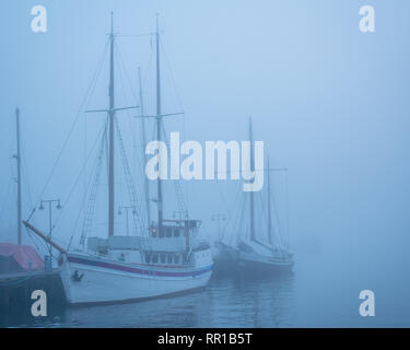 Misty romantico di imbarcazioni a vela senza vele in acqua vicino a un dock Foto Stock