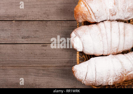 Croissant spolverati con zucchero a velo sul vecchio sfondo di legno con una copia dello spazio per il tuo testo. Vista superiore Foto Stock