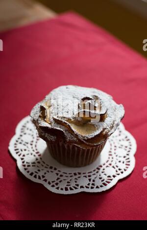 Un unico vegan muffin apple spolverato di zucchero a velo, su un centrino e tovaglia rosso. Foto Stock