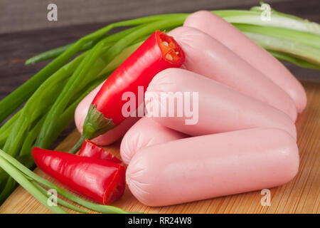 Cumulo di salsicce con cipolline e peperoncino su un tagliere con sfondo di legno Foto Stock