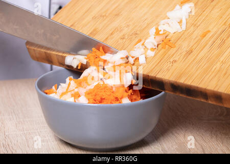 Lo Chef riversa schiacciate le cipolle e le carote in una ciotola Foto Stock