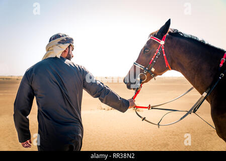 Medio Oriente uomo bello con il tipico abito emirates in sella ad un cavallo arabo nel deserto di Dubai Foto Stock