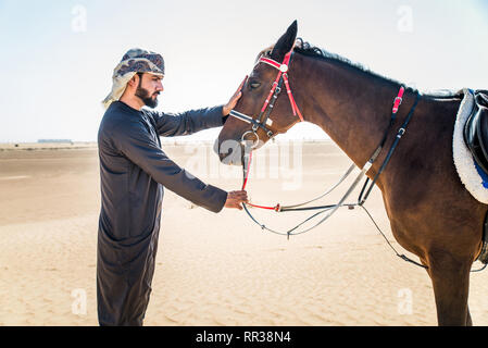 Medio Oriente uomo bello con il tipico abito emirates in sella ad un cavallo arabo nel deserto di Dubai Foto Stock