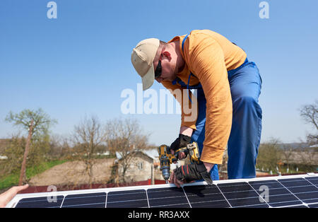 Ingegnere maschio installazione stand-alone solare pannello fotovoltaico sistema utilizzando un cacciavite. Elettricista blu montaggio modulo solare sul tetto di casa moderna. L'energia alternativa concetto ecologico. Foto Stock