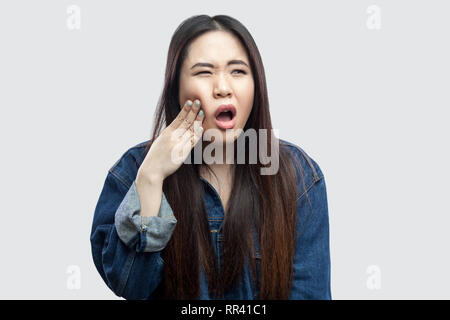 Mal di denti. Ritratto di malati bella bruna asian giovane donna casual in denim blu con camicia con il trucco permanente e tenendo il suo dente doloroso. indo Foto Stock