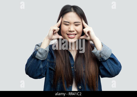 Mal di testa o di pensare. Ritratto di triste bella bruna asian giovane donna casual in denim blu con camicia con il trucco permanente e la tiene il capo. indo Foto Stock