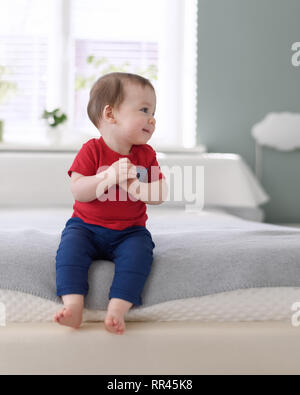 Happy baby boy in maglietta rossa sul letto nella sua camera Foto Stock