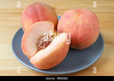 Due nuove pesca matura i frutti interi e un taglio Peach su una piastra blu servita su un tavolo di legno Foto Stock