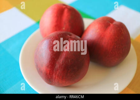 Tre fresche e mature le pesche noci frutti interi sulla piastra bianca servita su colori brillanti tovaglia Foto Stock