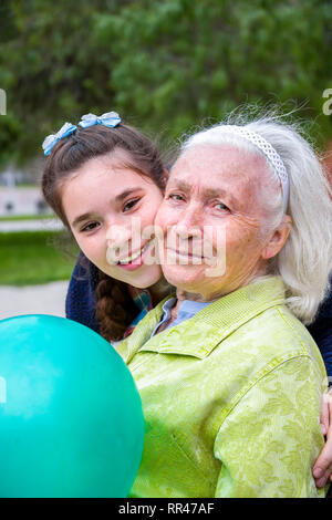 Bella ragazza abbraccia il suo bellissimo grey-haired nonna. Un piacevole donna anziana si siede su una panchina nel parco tenendo un palloncino ed entrambi hanno sorriso happ Foto Stock