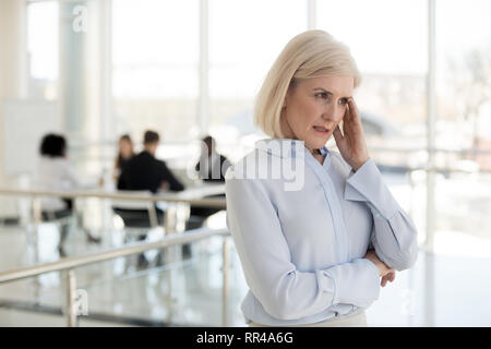 Imprenditrice di età soffre di mal di testa in piedi nel corridoio di office Foto Stock