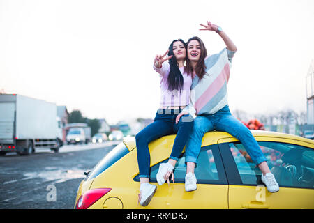 Migliore Femmina amici tifo in auto road trip al tramonto. Le persone felici outdoor in vacanza tour. Il concetto di amicizia a viaggiare con nostalgico positivo Foto Stock