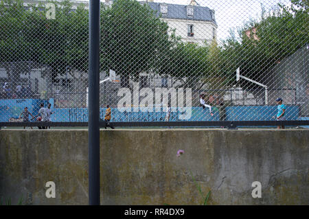 I bambini e gli adolescenti giocano e si ritrovano nel campo da calcio recintato, Square Léon, Rue des Gardes, Goutte d'Or, 75018, Parigi, Francia Foto Stock