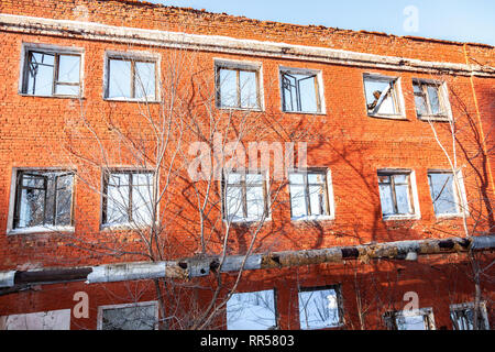 Vecchio abbandonato e distrutto edificio di mattoni rossi con finestre rotte contro un cielo blu in giornata invernale Foto Stock