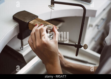 Master la mano. Close up di un gioielliere femmina le mani lavorando su un anello al suo banco. Gioielleria processo. Business. Workshop di gioielli. Foto Stock