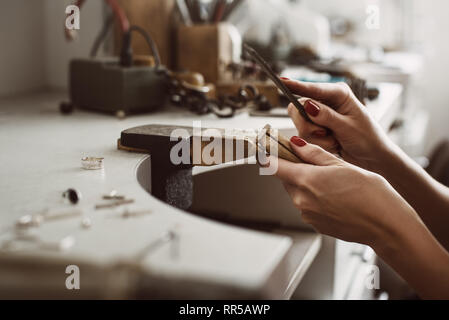 Master con le mani in mano. Vista laterale di un gioielliere femmina mani creando un anello d'argento presso il suo banco di lavoro. Rendendo gli accessori. Gioielleria processo. Gioielli dotare Foto Stock