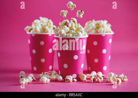 Gustoso il popcorn cadere in tazze sullo sfondo rosa. Fresca salata croccante di popcorn fatti in casa in rosa bicchieri di carta. Foto Stock