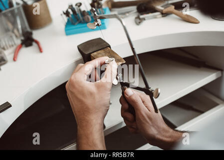 Fiducioso del moto. Close-up foto del gioielliere le mani facendo un anello color argento con professional gioielliere regolabile la sega a telaio il suo banco di lavoro Foto Stock