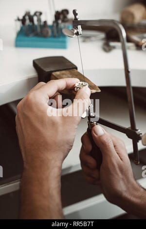 Gioielliere con le mani in mano. Close-up foto del gioielliere le mani facendo un anello color argento con professional gioielliere regolabile la sega a telaio il suo banco di lavoro Foto Stock
