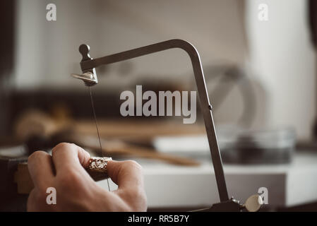 So quello che sto facendo. Close-up foto del gioielliere le mani facendo un anello color argento con professional gioielliere regolabile la sega a telaio il suo banco di lavoro Foto Stock